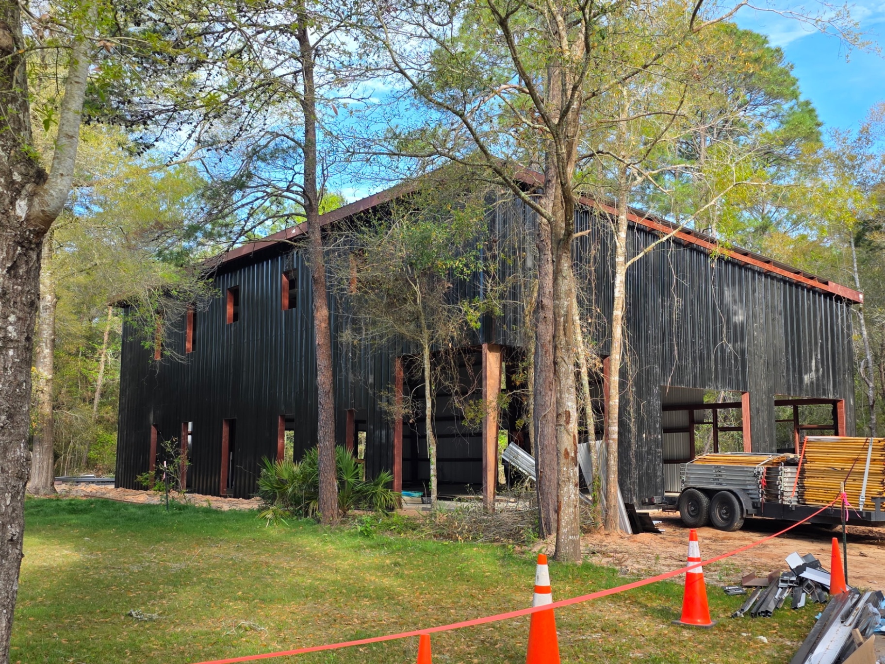 Black steel pole barn with red trim under construction in the woods